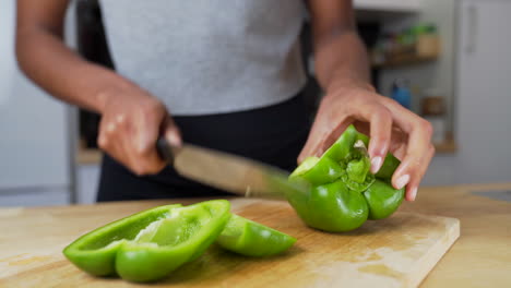 Dunkelhäutige-Frau,-Die-Eine-Grüne-Paprika-Auf-Einem-Holzschneidebrett-In-Stücke-Schneidet