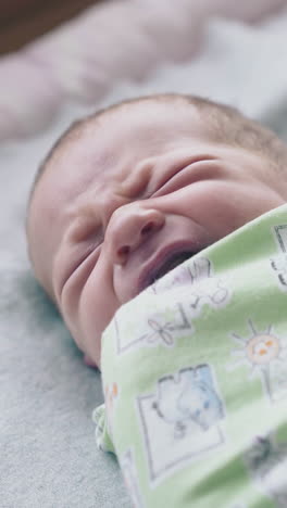 adorable newborn baby lies with closed eyes wrapped in muslin swaddle and starts crying close view slow motion