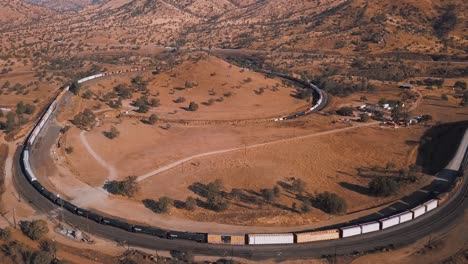 Aerial-view-of-long-freight-train-passing-through-Tehachapi-Loop,-California