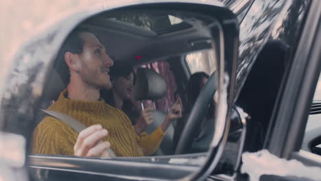 camera focuses on the rearview mirror of a car that reflects a family dancing while sitting inside a car