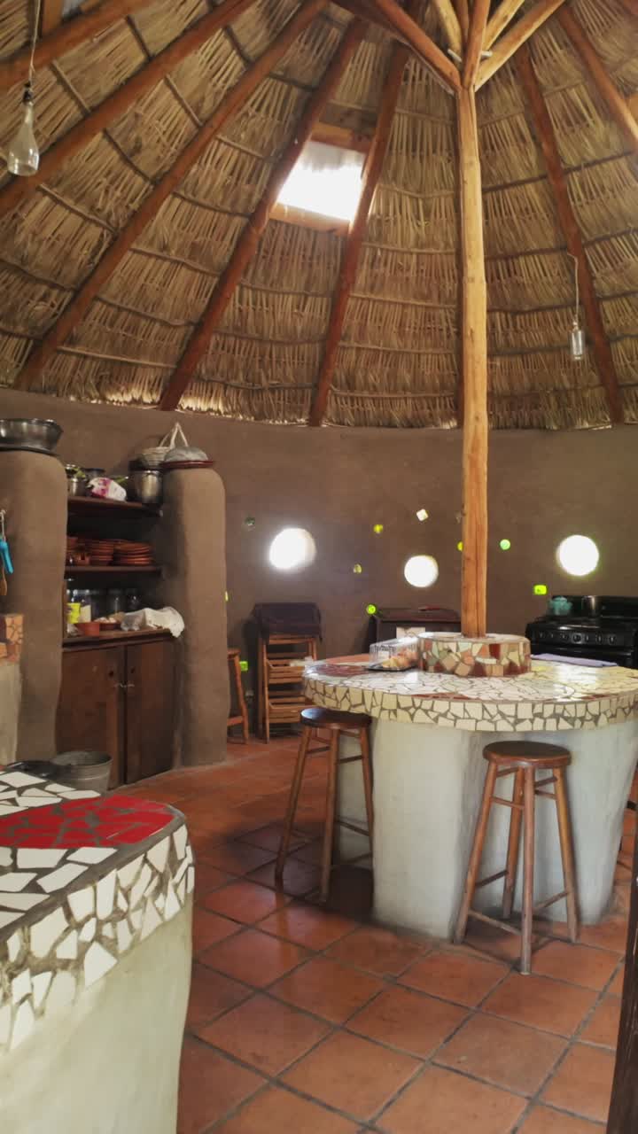 Rustic kitchen with thatched ceiling, mosaic counter, and round windows, vertical shot