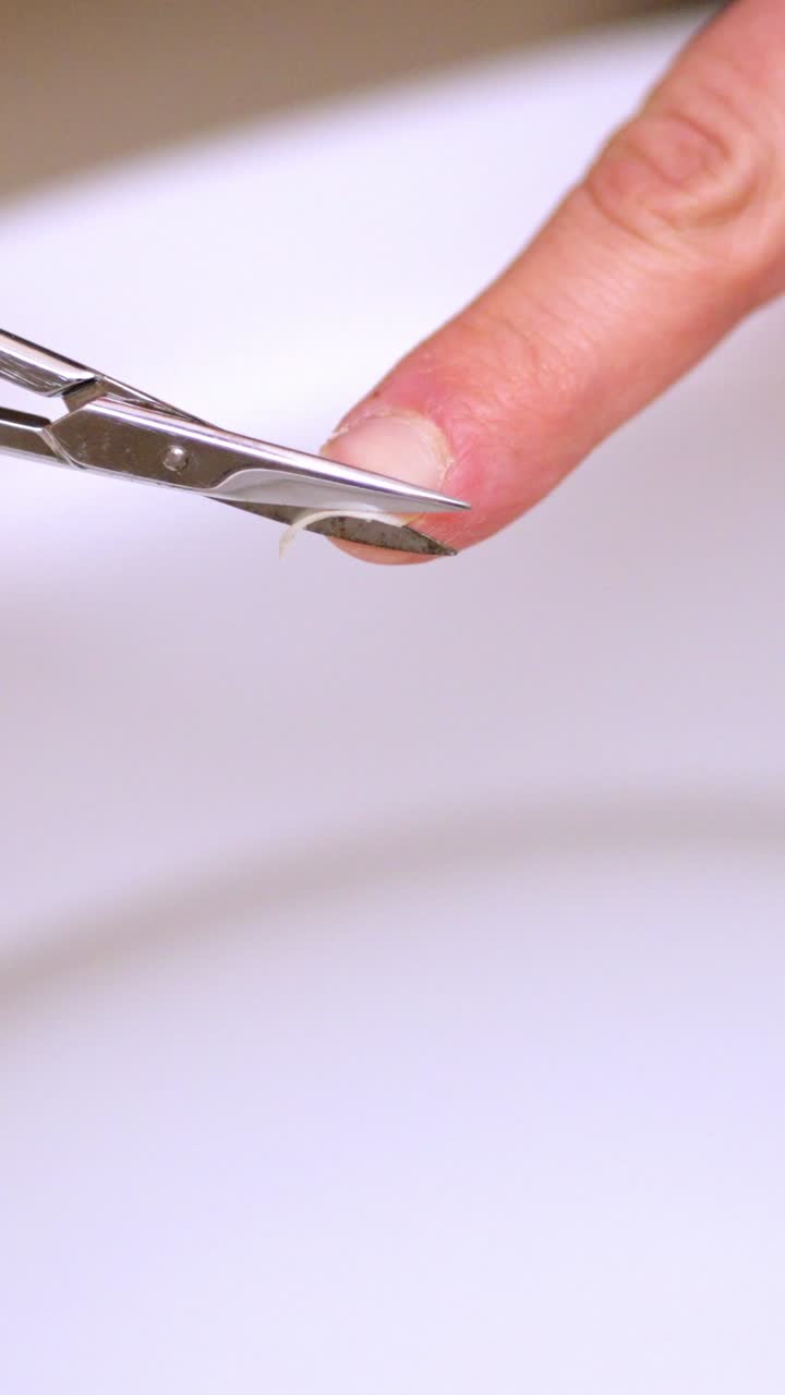 Manicure, cutting fingernails with nail scissors over toilet