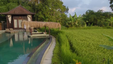 A-luxurious-poolside-villa-set-amidst-vibrant-green-foliage,-with-a-pristine-swimming-pool-and-charming-thatched-pavilions,-emphasizing-the-peaceful-and-idyllic-ambiance