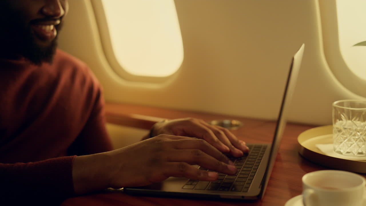 Smiling guy chatting laptop at airplane window closeup. Happy passenger typing
