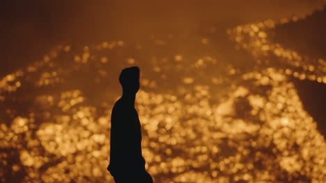 pacaya volcano, guatemala - a silhouette of a man wearing a headlamp standing near the flowing rivers of lava - handheld shot