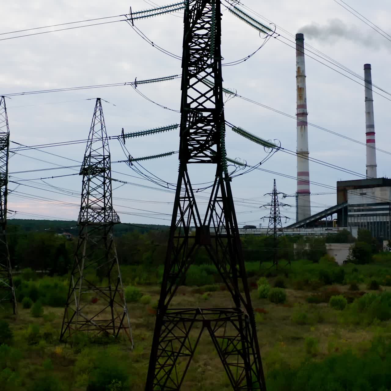 High-voltage electric tower. Transmission lines on the background of industrial factory. Steel power pylons on field in the countryside. Camera rising up.