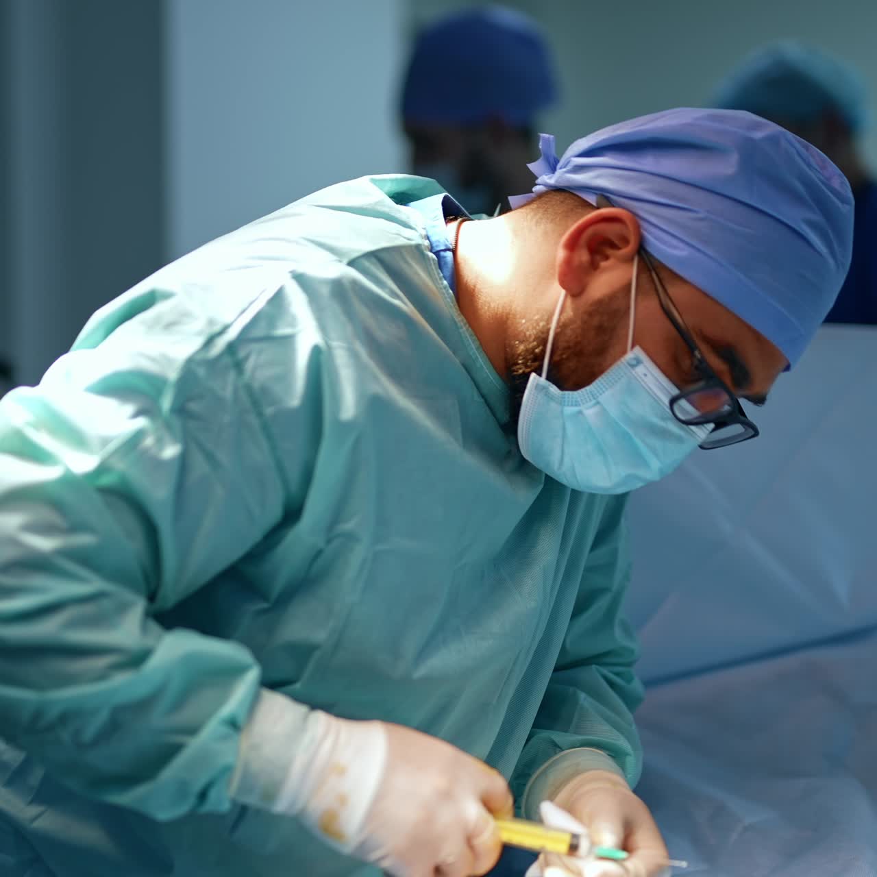 Careful focused anesthesiologist giving injection to the patient. Doctor holding a syringe bent over the person on surgical table