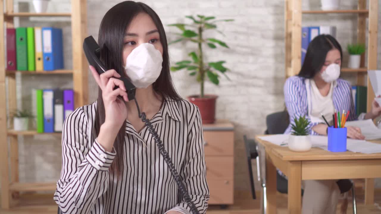 두 명의 젊은 아시아 소녀 사무실 직원이 사무실에서 일하는 얼굴에 보호 의료 마스크를 착용합니다.