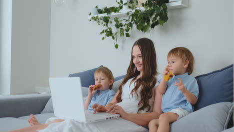 Young-beautiful-mother-and-two-young-children-sitting-on-the-couch-looking-at-the-laptop-screen-and-make-online-purchases