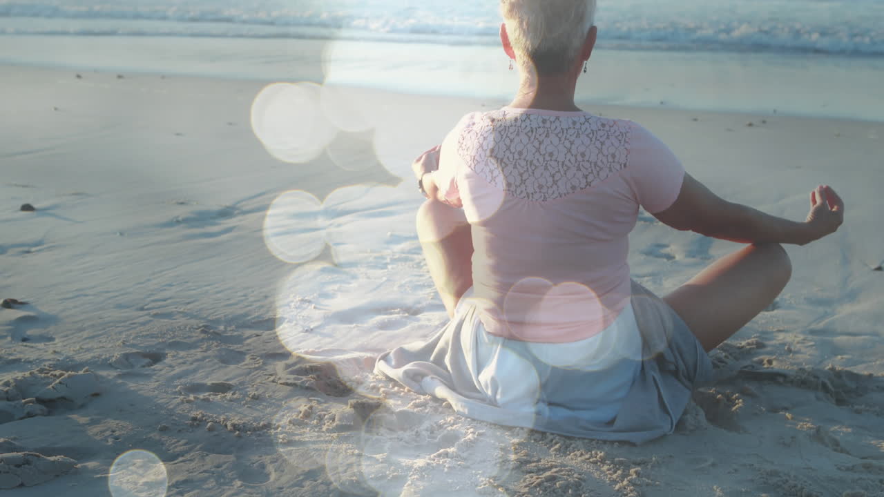animación de puntos de luz sobre una mujer caucásica mayor practicando yoga en la playa y meditando