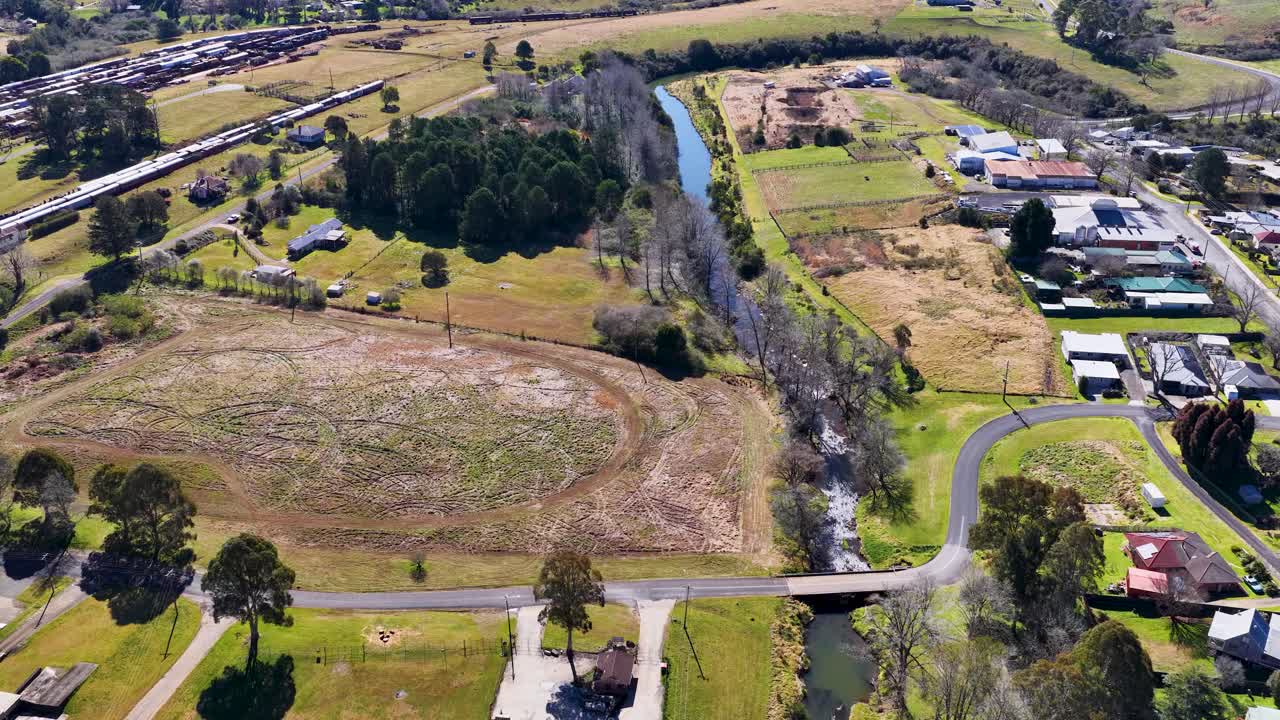 Drone ascends above rural Dorrigo, revealing farmland, creek, roads, and small town buildings in sunlight