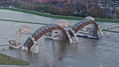 Zoomed in and orbit drone shot moving away from the weir of Driel during high water levels with a cargo ship passing thru