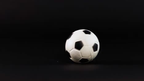 a soccer ball moves smoothly across a dark, flat background, showcasing its motion and rotation.