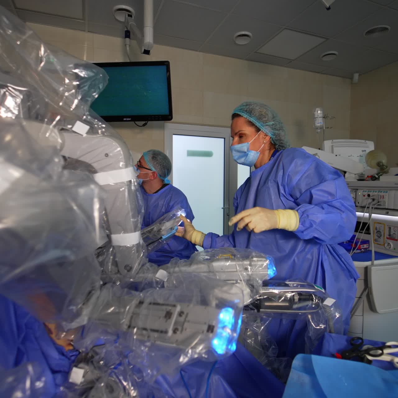 Medics and robotic equipment working in the surgery room. Female medic moving the robotic arms and looks at the screen
