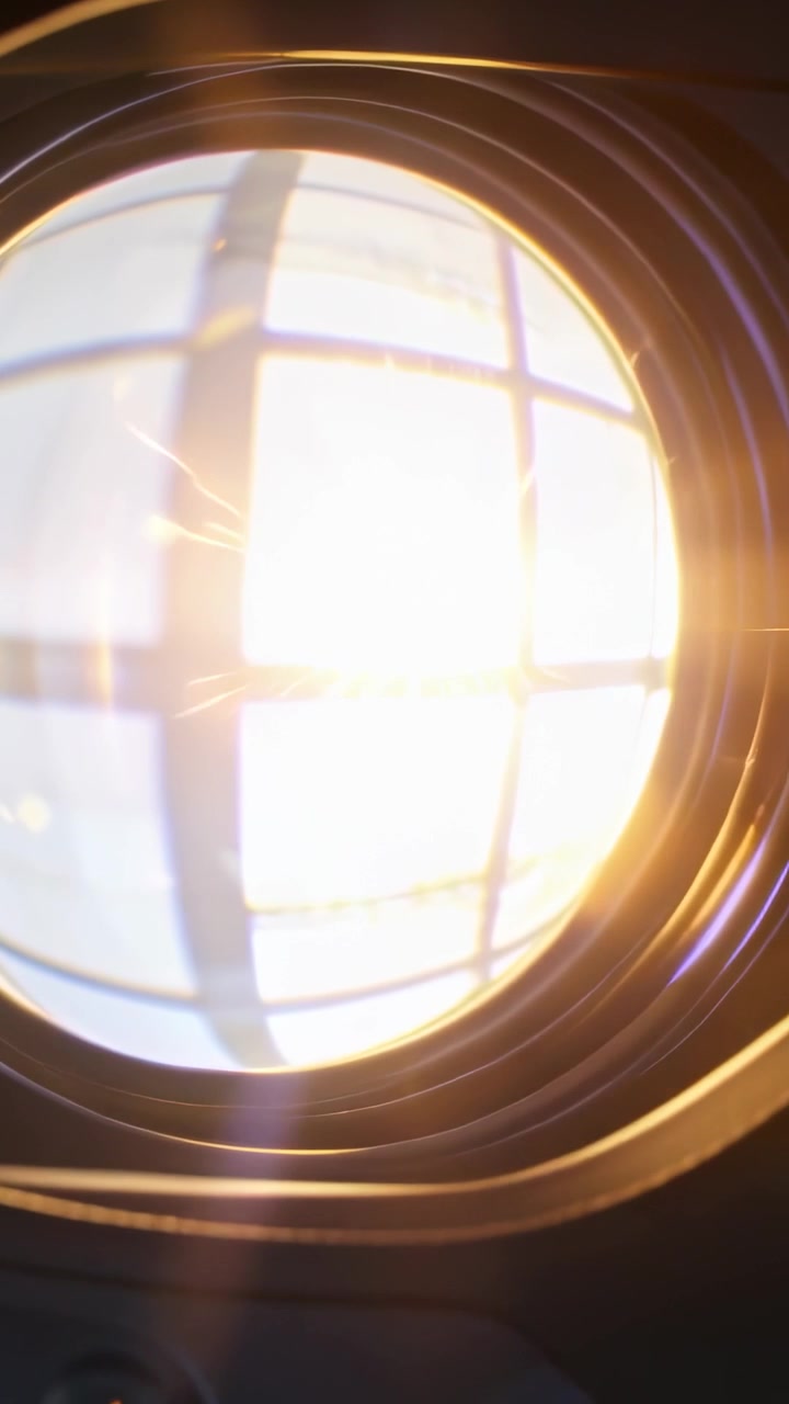Vertical video: Sunlight striking circular lens at window, making grid reflection and orange flare