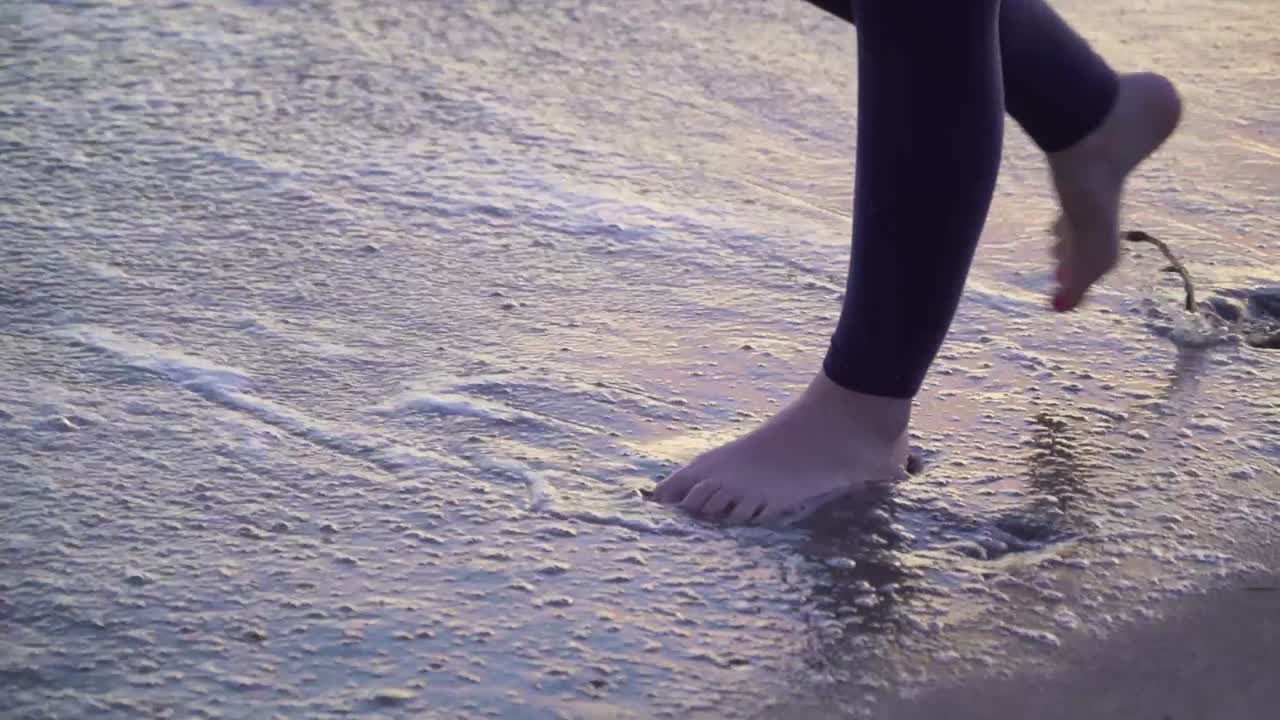 Piedi di donna che camminano nell'acqua sulla spiaggia al tramonto.