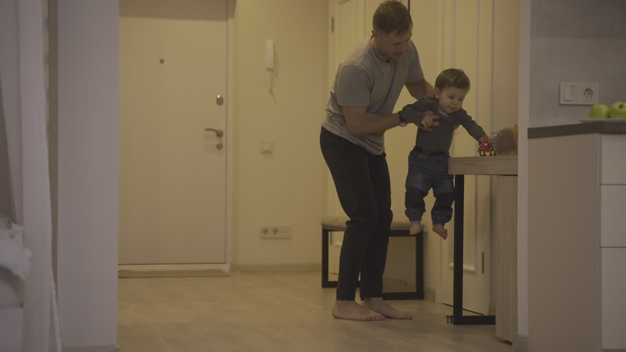 padre ayudando a su bebé a dar sus primeros pasos desde el pasillo hasta la sala de estar en casa