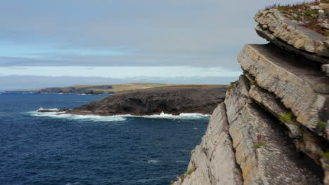 Forwards-fly-around-rock-block.-Revealing-panoramic-view-of-sea-coast-and-rippled-blue-sea.-Kilkee-Cliff-Walk,-Ireland