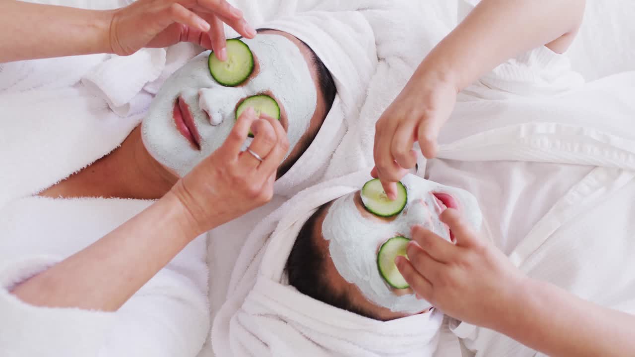 Video di madre e figlia asiatiche felici in accappatoi che fanno una maschera al cetriolo e si divertono.