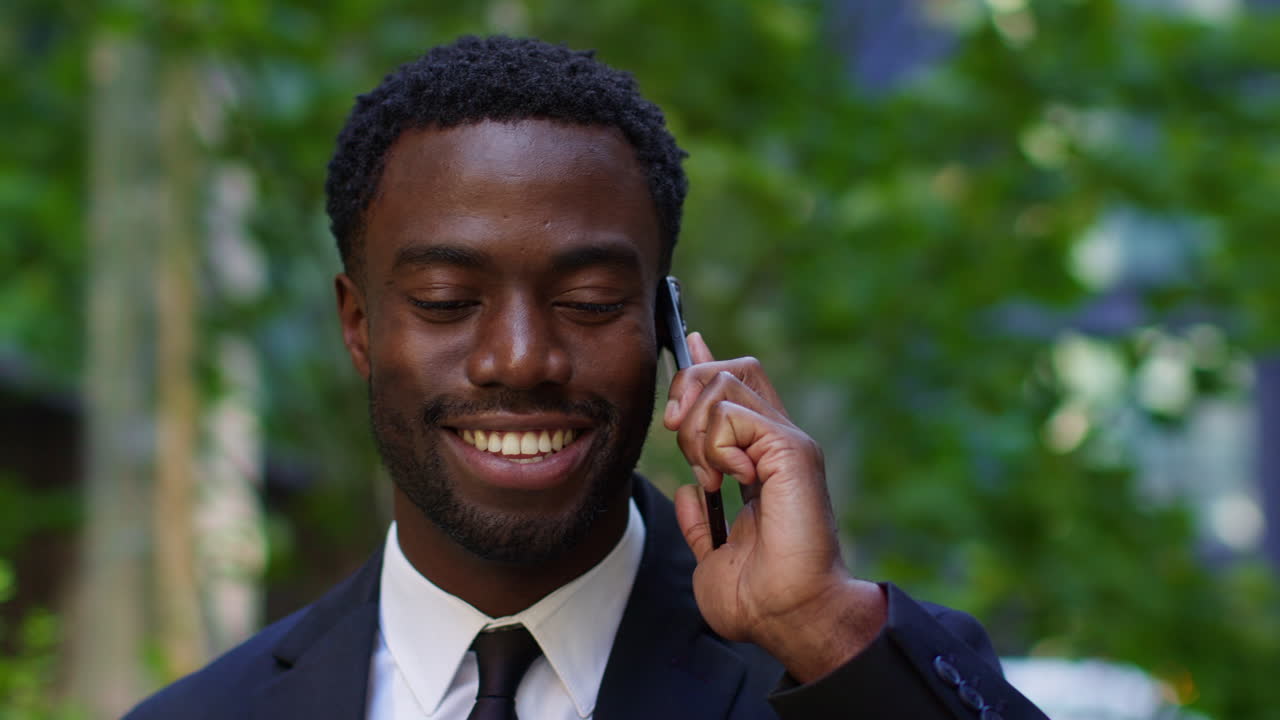 Close Up Of Smiling Young Businessman Wearing Suit Talking On Mobile Phone Standing Outside Offices In The Financial District Of The City Of London UK