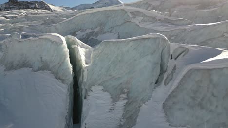 Aerial-view,-snow-covered-icy-peaks-of-a-glacier-and-crevasses,-sunny-day