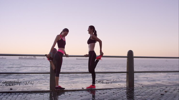 Two athletic friends stretching before a run on promenade at sunset
