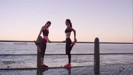 Zwei-Sportliche-Freunde-Dehnen-Sich-Vor-Einem-Lauf-Auf-Der-Promenade-Bei-Sonnenuntergang