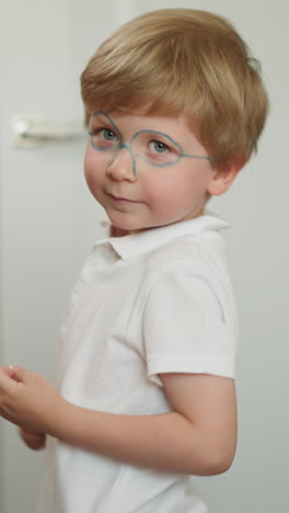 little boy dances standing in light room. child with painted glasses wiggles bottom and waves hands. preschooler has fun making funny body movements