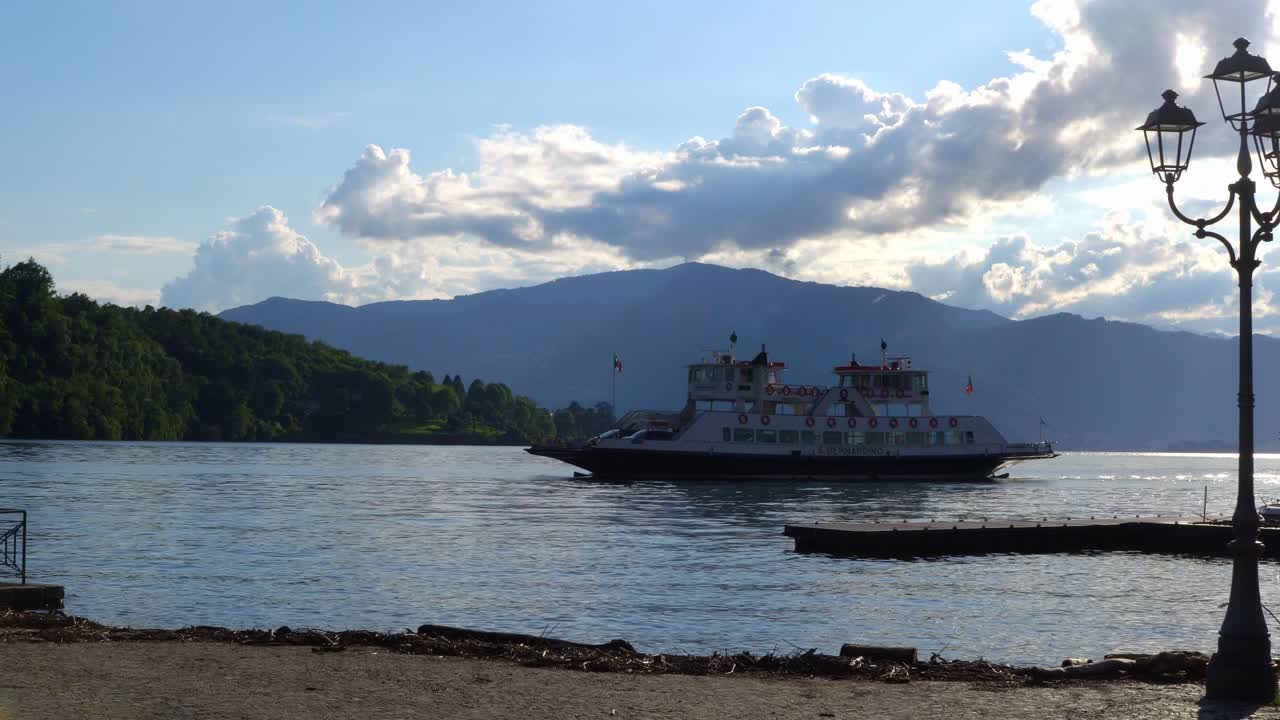 마조레 호수 (lake maggiore) 에 있는 페리 보트 (ferry boat) 가 해가 지는 동안 이탈리아 바레세 주 라베노-몬벨로 (laveno-mombello) 에 접근하고 있다.