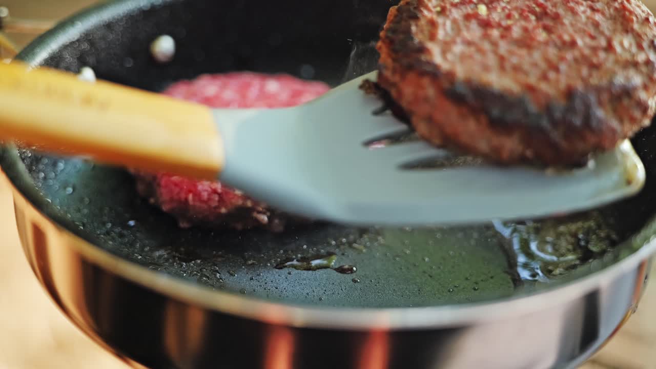 Burger sizzles with smoke and oil as spatula flips it in warm evening light