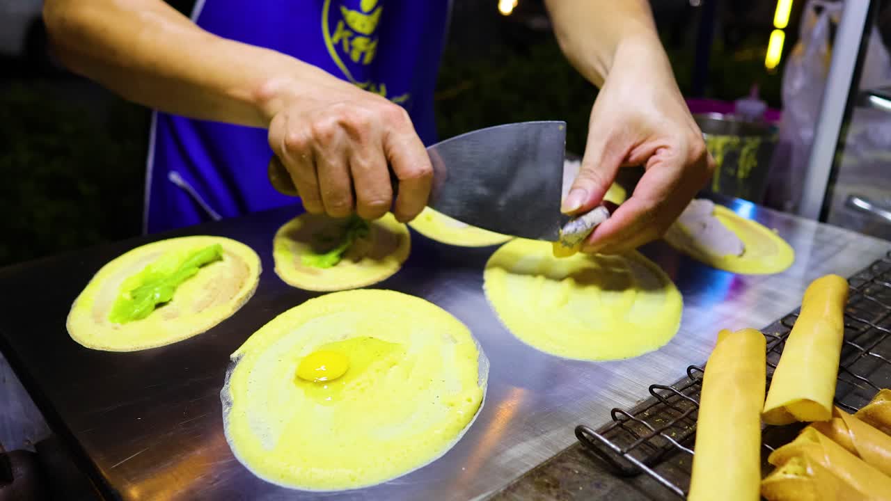 A street vendor expertly prepares traditional crispy pancakes in Bangkok, Thailand, under bright lighting, showcasing vibrant colors and skilled technique