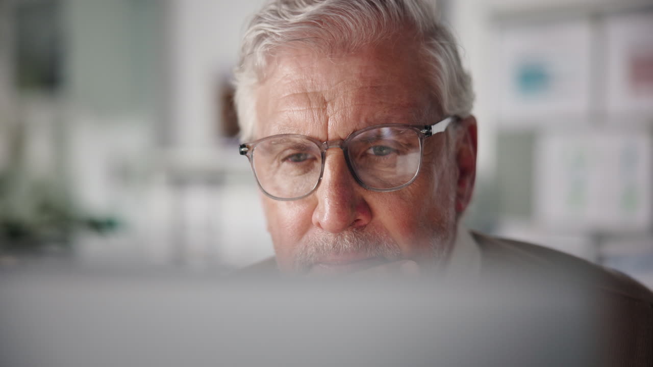 Close-up of an elderly man with glasses using a computer