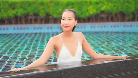 front view of smiling happy asian lady in a swimming pool wearing a white bikini