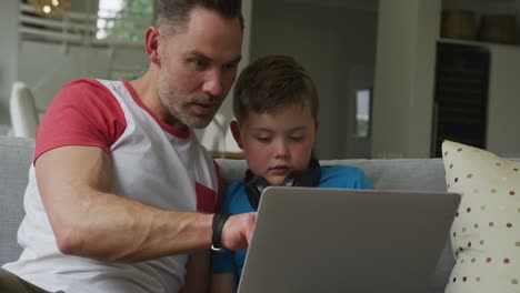 padre caucásico con hijo sentado en la sala de estar y usando una computadora portátil