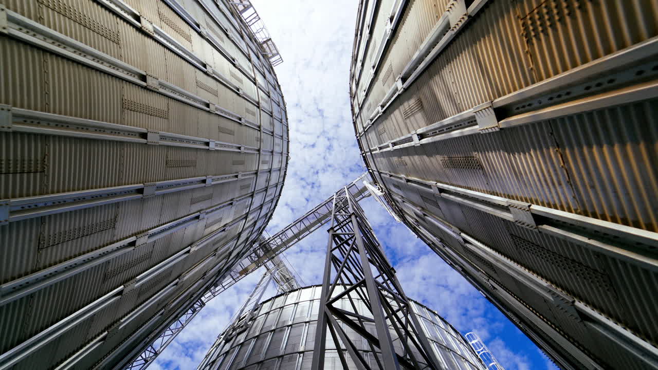 Modern grain terminal. Metal storage tanks for drying grain. Industrial equipment for agribusiness. Large grain elevators on blue sky background. Close-up.