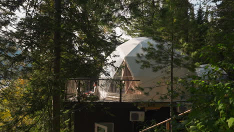 glamping dome tent with terrace in pine wood. tourists enjoy calmness meditating on ground by semi spherical house. comfortable travel to wild nature