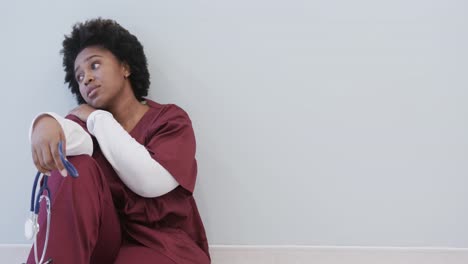 Tired-african-american-female-doctor-sitting-in-hospital-corridor-with-copy-space,-slow-motion