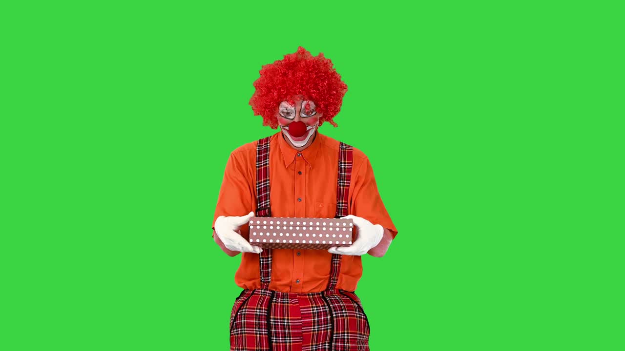 un payaso macho feliz sosteniendo un regalo y caminando en una pantalla verde, llave de croma