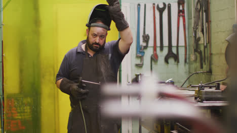 trabajador de fábrica caucásico en una fábrica que se quita una máscara de soldadura, sosteniendo una pistola de soldadura