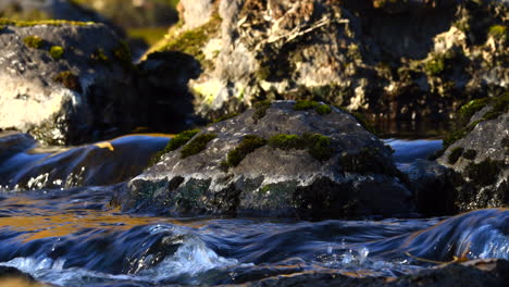 tripod shot of a group of mossy rocks in a river in autumn