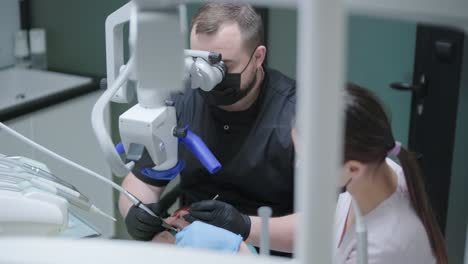 male dentist working with dental microscope in modern stomatology clinic. doctor using microscope for root canal treatment. stomatologist performs a surgical operation. cosmetic dentistry and surgery.