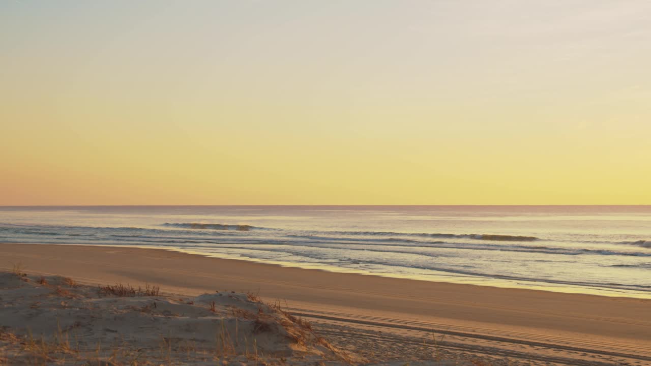 vista de las olas y la playa desde la duna de arena durante los tonos amarillos coloridos del atardecer