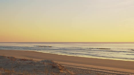 view of the waves and beach from sand dune during colorful yellow tones sunset