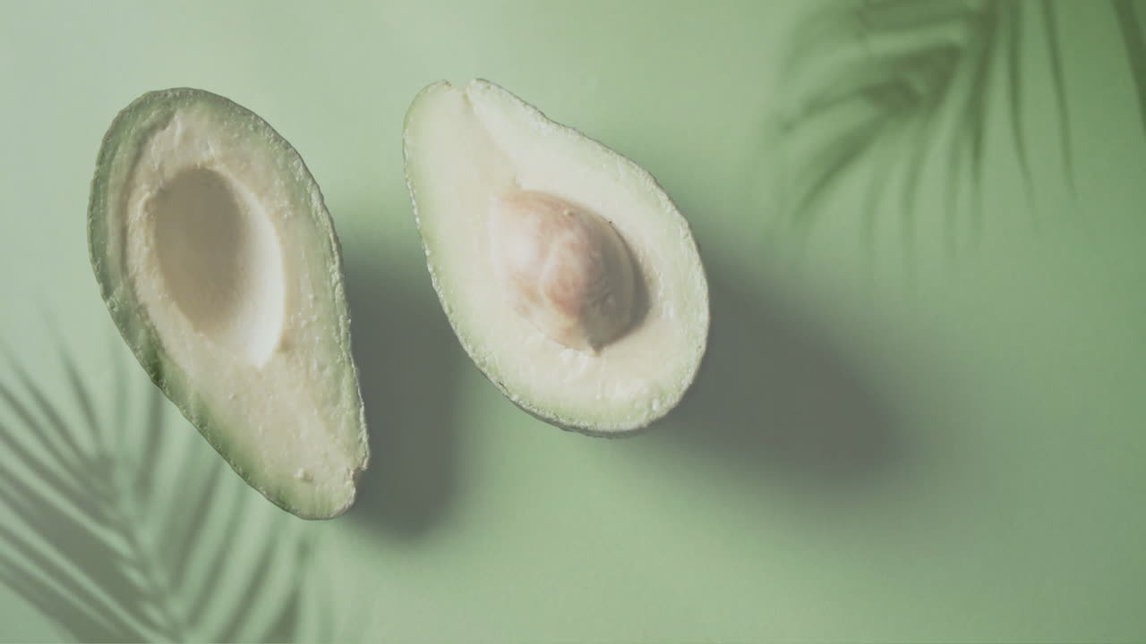 Animazione di foglie di palma su un avocado tagliato a metà su sfondo verde