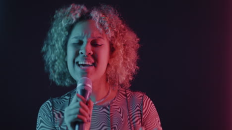 woman singing into microphone under colorful studio lights