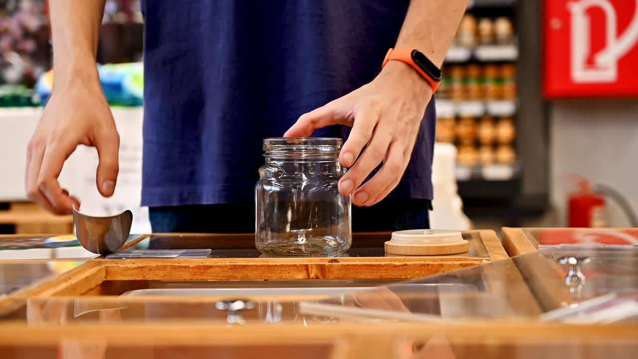 Man's hands filling a glass jar with nuts, dried fruits and berries in supermarket. Ecology idea
