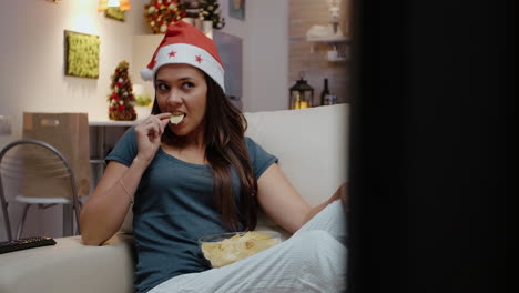 mujer con sombrero de santa y mirando una película en la televisión
