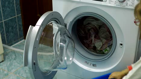 girl child takes the clean clothes from the washing machine. daughter helps her mother house affairs. video shooting closeup.