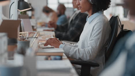 mujer de negocios joven usando computadora escribiendo en el teclado enviando correos electrónicos conectándose en línea en una oficina ocupada usando auriculares