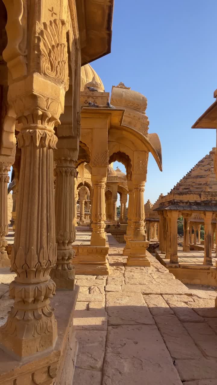 A close-up pan view of Jaisalmer's Bada Bagh on a bright desert day, highlighting its stunning Rajasthan architecture, detailed stone carvings, domed cenotaphs, and serene golden ambiance.